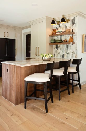 Kitchen interior with barstools at a wood island, beige cabinets, black fridge, and decorative open shelving.