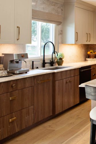 Kitchen counter with walnut cabinets, light stone backsplash, black faucet, and an espresso machine beside the window.