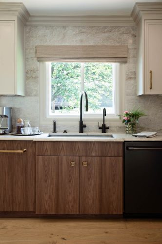 Kitchen sink area with wood cabinets, black faucet, stone backsplash, and countertop espresso machine.