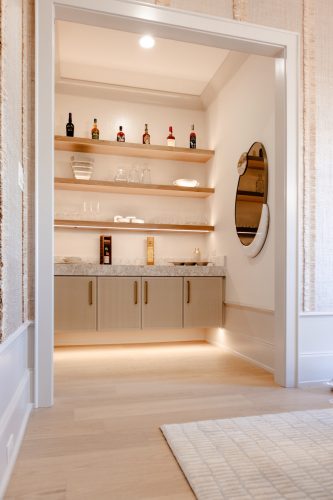 Wine room with pale oak hardwood floors, white shaker-style cabinets, brass pulls, farmhouse sink, and quartz countertops in a bright natural light setting.