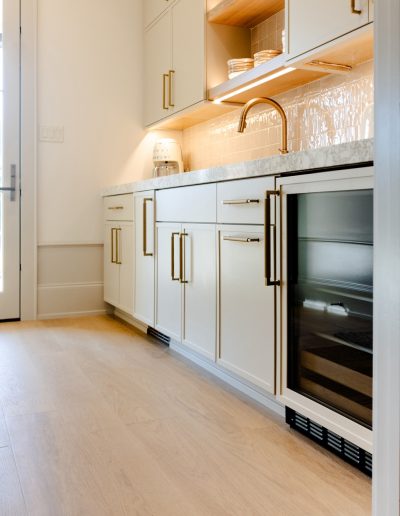 Minimalist kitchen with soft white cabinetry, matte gold hardware, and natural oak flooring adding warmth and texture.