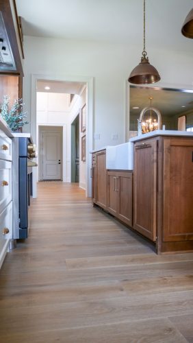 Stylish kitchen interior featuring transitional wood cabinets, a farmhouse apron sink, and light flooring leading toward a bright entryway.
