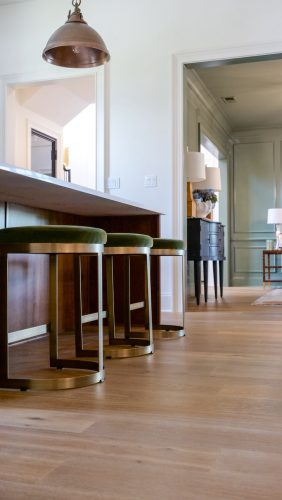 Kitchen island with modern green velvet stools and warm hardwood floors, opening into a softly lit hallway.