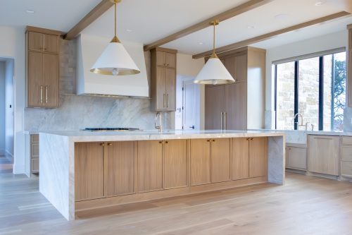 Warm modern kitchen with light wood cabinetry, marble waterfall island, and wide-plank hardwood flooring