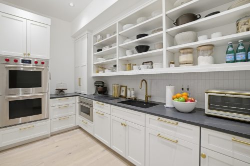 Custom second kitchen with white cabinetry and light wood flooring.