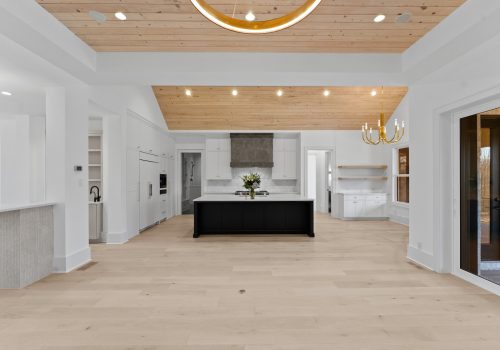 Modern kitchen with white cabinetry, black island, brass pendant lights, and natural wood ceiling above light wood flooring.