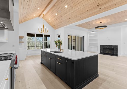 Open kitchen and dining area with wood ceiling, brass chandelier, black island seating, and light hardwood floors.