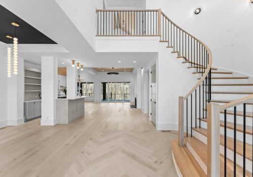 Two-story entry with custom herringbone wood flooring by FloorMade leading into open living and kitchen spaces in this Charlotte luxury home.