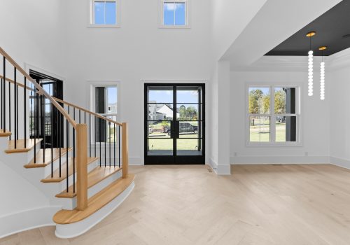 Open double glass doors reveal a bright foyer with a custom herringbone wood floor in a modern two-story entry.