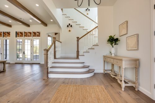 Curved staircase and neutral interior grounded by warm brown wood flooring.