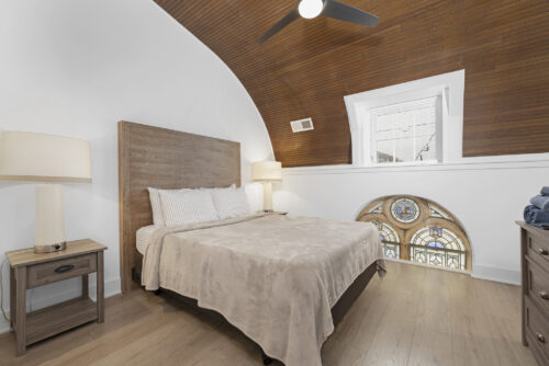 Bedroom with arched ceiling and wood paneling above wide plank flooring
