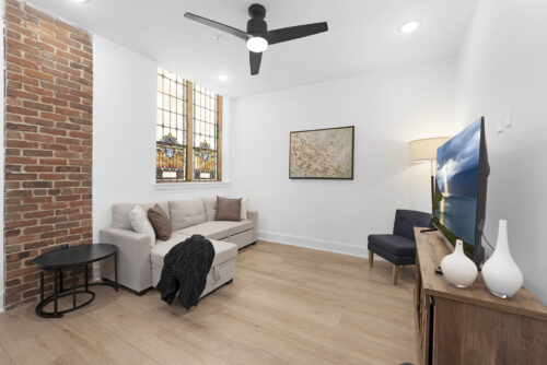 Open living room with brick detail, stained glass, and flooring connecting to kitchen