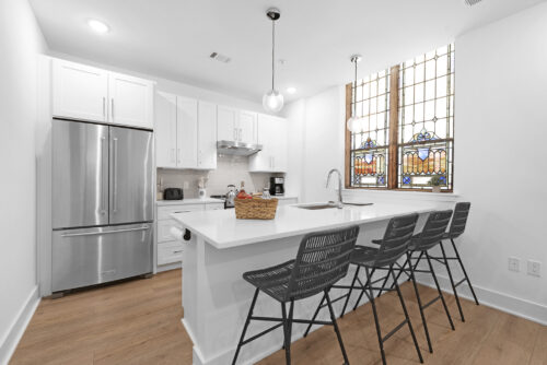Bright kitchen with white cabinets and stained glass window over wide plank flooring in Charlotte condo