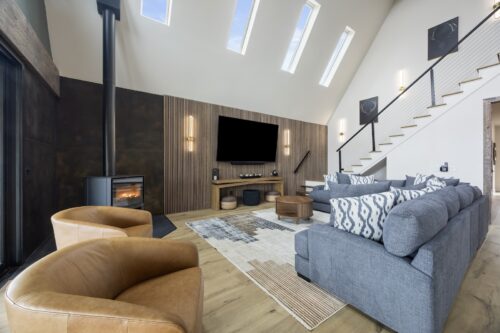 A-frame living room with vaulted ceilings, wood slat wall, and natural-toned wood flooring overlooking a lake