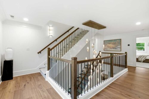 Open staircase with preserved millwork, iron railing, and wide plank hardwood flooring.