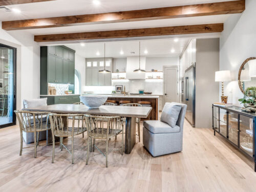 Open-concept kitchen with light oak floors, natural wood cabinetry, and dark ceiling beams