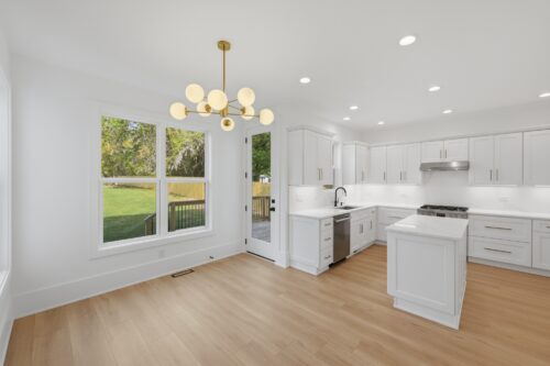 Extra-wide plank flooring connecting a white kitchen and light-filled dining space