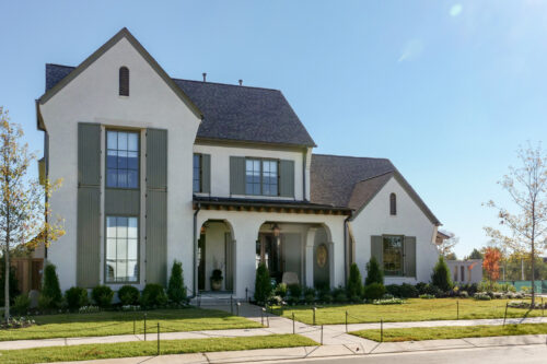 Exterior of a luxury Collierville residence with white stucco, muted green shutters, and a welcoming arched entryway.