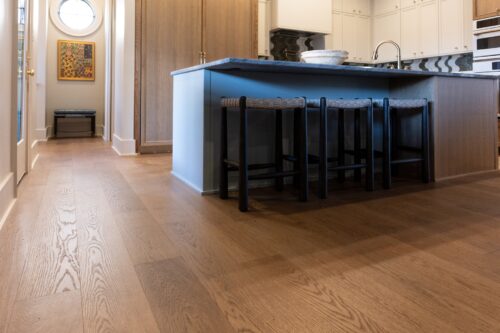 A designer kitchen features warm European white oak floors, contrasting cabinetry, and a bold black-and-white patterned backsplash.