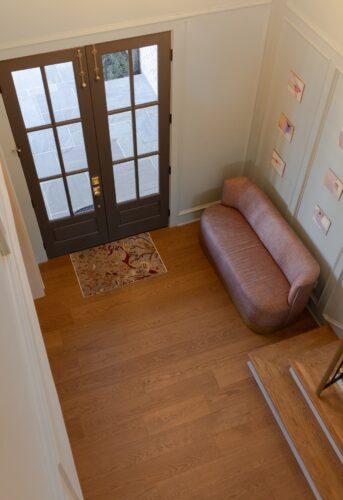 Warm European white oak flooring anchors a dramatic Collierville entryway with paneled walls, dark double doors, and a mauve upholstered settee.