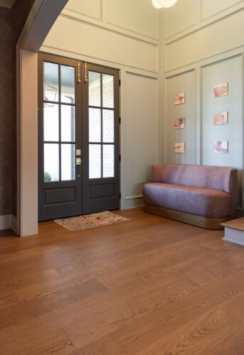 A welcoming entryway features natural European white oak flooring, dark double doors, brass hardware, and sculptural seating.