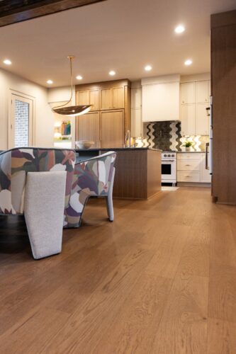 A Collierville dining room pairs warm oak hardwood flooring with playful multicolored chairs, a glass dining table, and modern kitchen finishes.