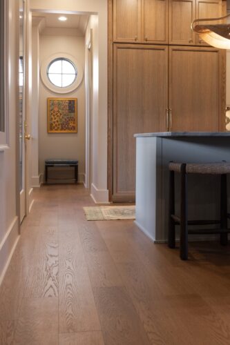 Wide plank European white oak flooring complements natural wood cabinetry, a dark kitchen island, and woven barstools in this Collierville home.