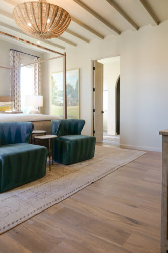 Silvian Luonto wide plank European white oak flooring complements teal velvet chairs and exposed ceiling beams in a Collierville bedroom.