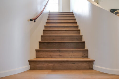 Warm brown hardwood staircase with matching wide plank European white oak flooring and curved white architectural walls.