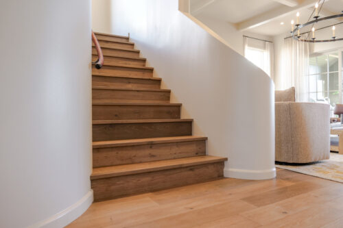 Wide plank oak flooring and matching wood stair treads complement soft white walls and natural light in a Southern-inspired home.